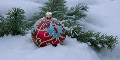 The primary subject of the image is a beautifully decorated Christmas ornament. The ornament is placed on a snow-covered tree, creating a festive and cozy atmosphere. The setting is a winter landscape, with snow covering the ground and trees. The visual style of the image is a combination of photo and digital art, as it captures the ornament's intricate details and the snowy environment. The colors and mood of the image are predominantly white and cold, with the ornament's red and